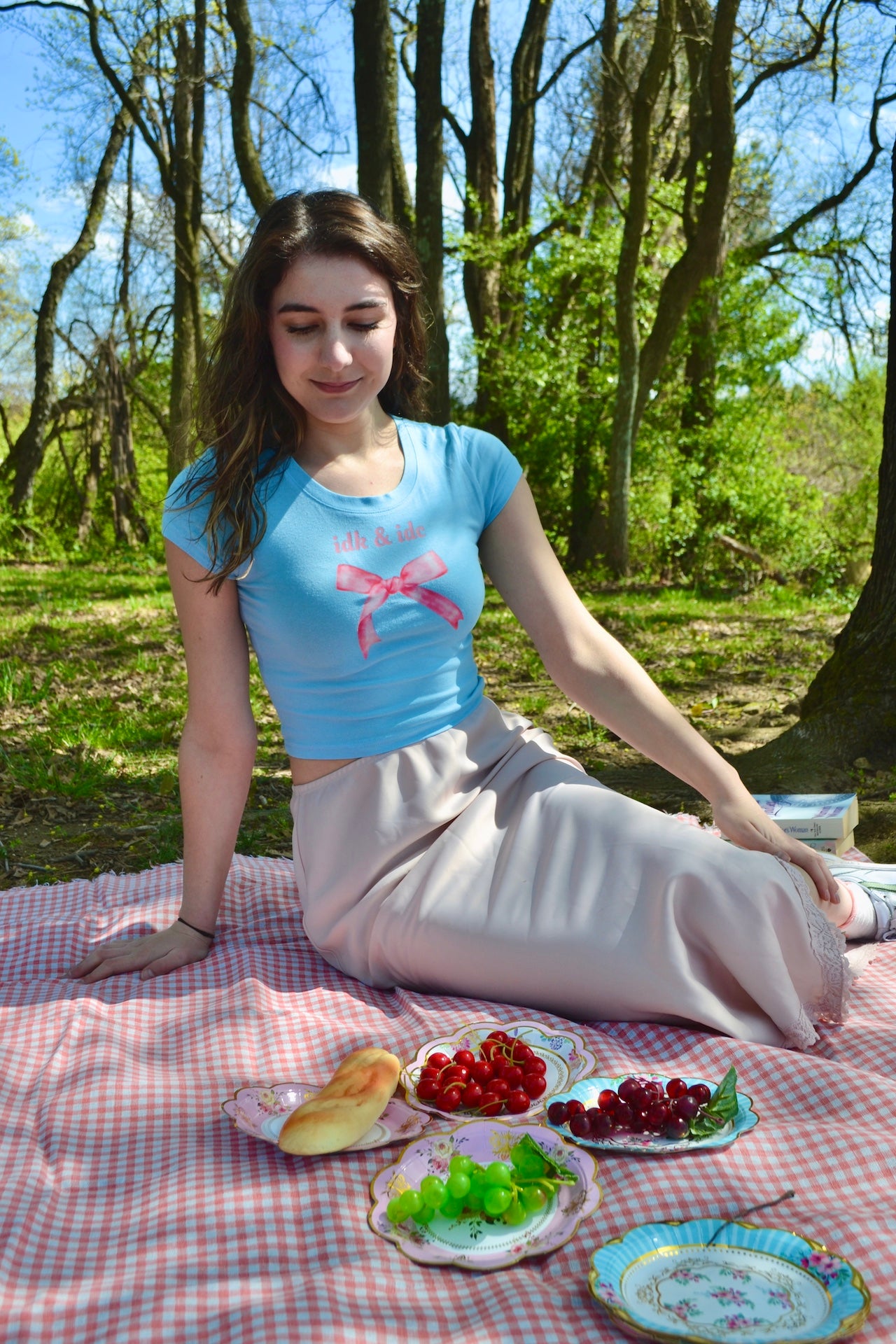a woman sitting on a picnic blanket with a plate of fruit