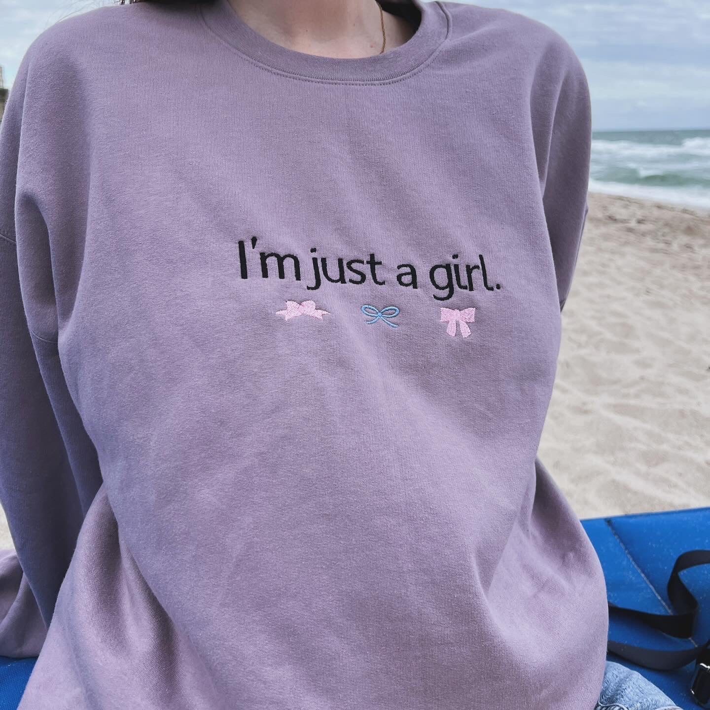a woman sitting on the beach wearing a sweatshirt that says i'm just a
