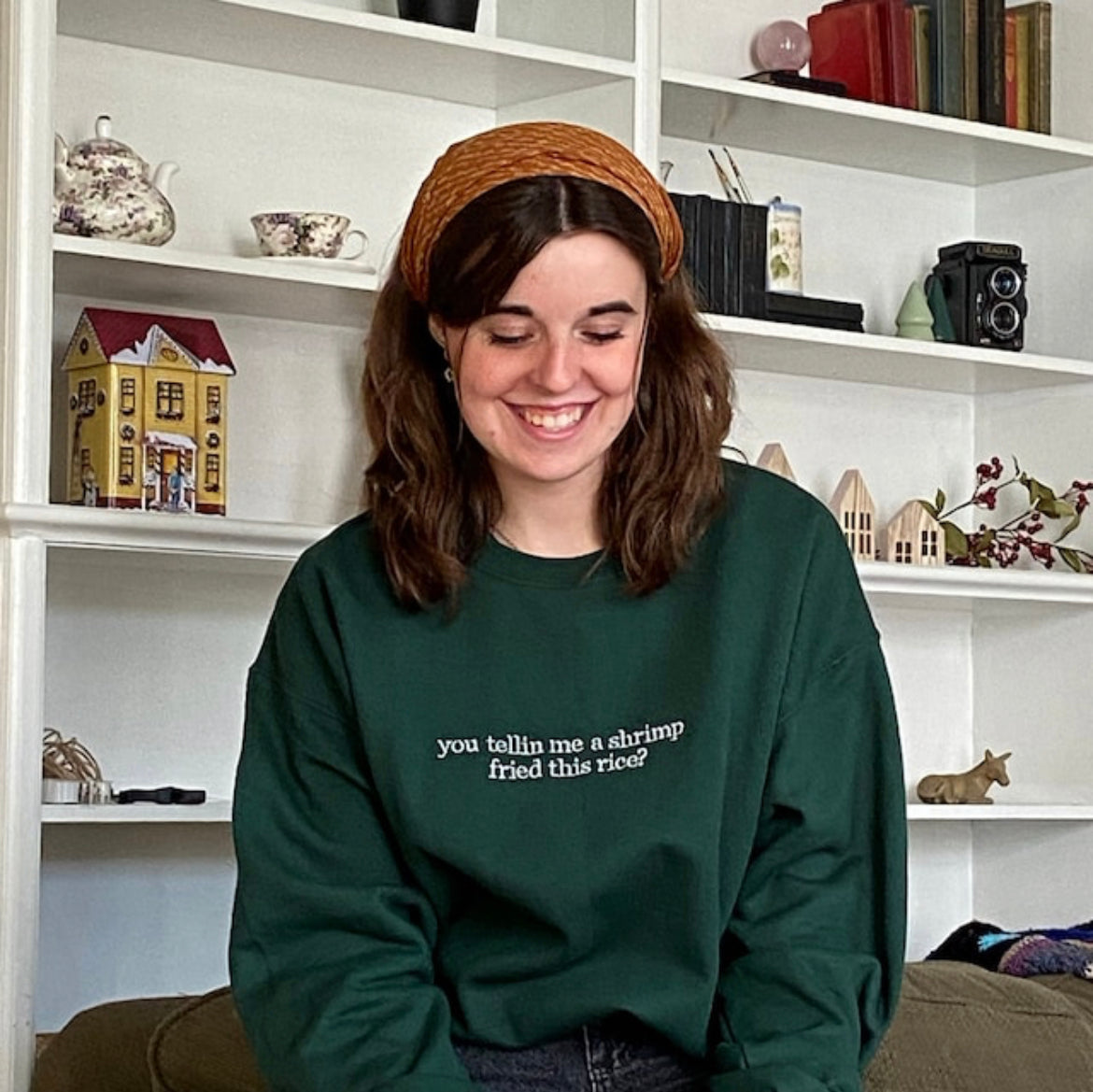 a woman sitting on a couch wearing a green sweatshirt